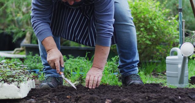 Content depicts a person bent over whilst working in a garden, using a gardening tool to plant or prepare the soil. Ideal for use in articles about gardening tips, outdoor hobbies, and healthy lifestyle content.