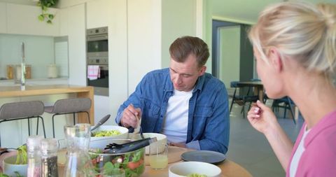 Couple sharing healthy salad dinner in modern bright kitchen with wooden island