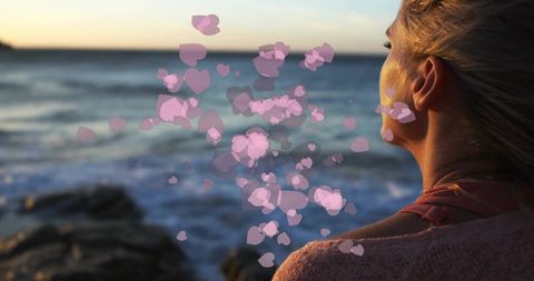 Woman in Pink Sweater Watching Sunset by Rocky Shore with Heart Overlays