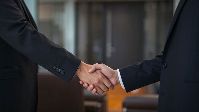 Shaking hands sealing corporate deal in modern office lobby showing suit cuffs