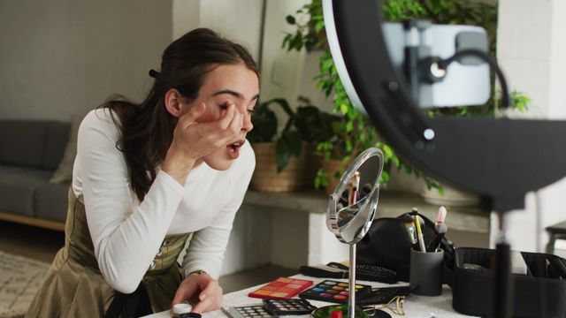 Perfect for themes promoting self-expression, inclusivity, and home lifestyle, this image shows a non-binary individual confidently applying makeup aided by a ring light. Utilizable for beauty tutorials or discussions on individual expression.