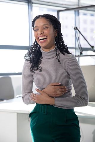 Laughing african american professional woman wearing turtleneck and rings in modern office