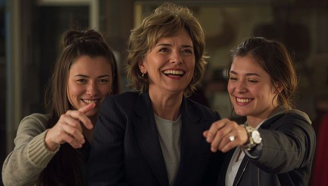 Three women laughing and pointing during cozy indoor gathering