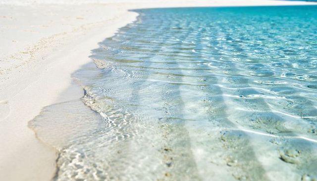 Crystal clear turquoise water lapping pristine white sand beach, calm sunlit shallow shore