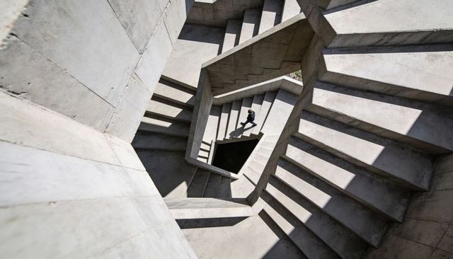 Brutalist Concrete Spiral Staircase Overhead with Man Descending and Diagonal Shadows