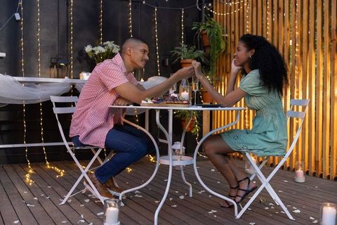 Intimate string-light patio dinner couples holding hands at candlelit bistro table