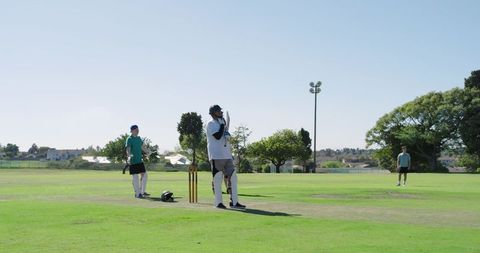 Diverse men playing cricket on suburban green with wooden stumps and helmet