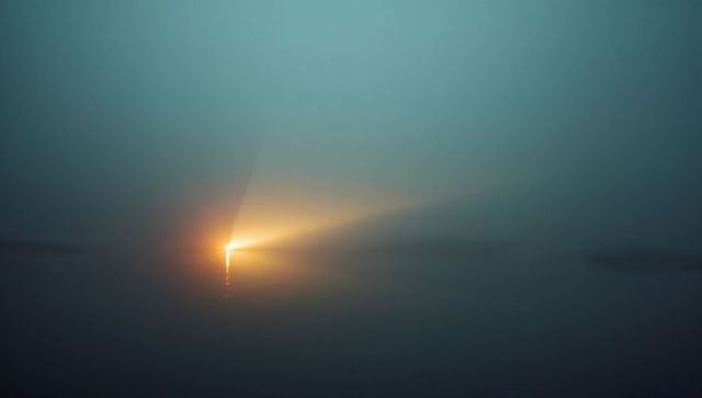 Mystical dawn light piercing foggy coastal waters with reflection