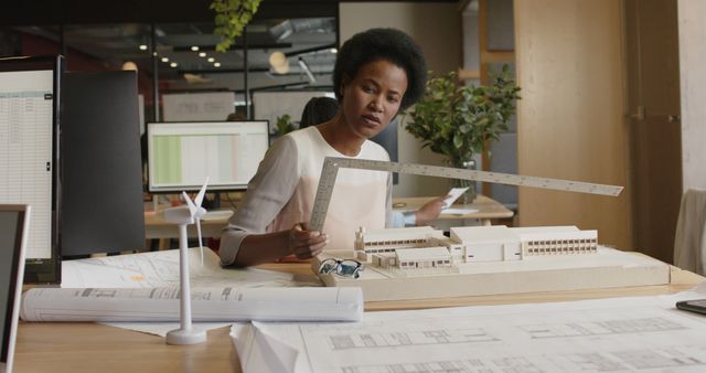 African american female architect using ruler and looking at building model at office. Office, business, architecture, design and work, unaltered.