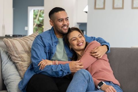 Young couple embracing on couch in modern open-plan living room, cozy home romance