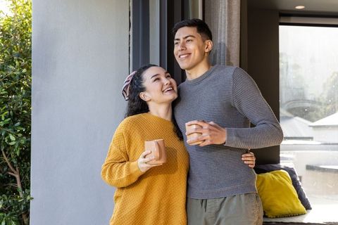 Cozy couple enjoying morning coffee on doorstep by sliding glass doors with garden view