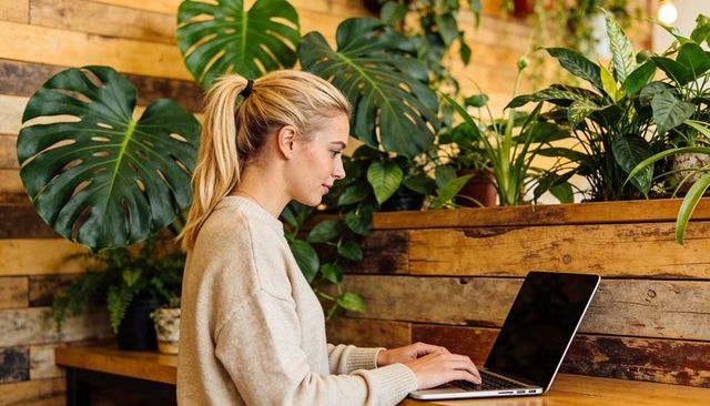 Young woman working on laptop at plant-filled café counter cozy coworking workspace