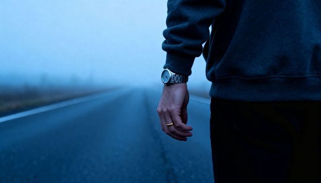 Standing on foggy road wearing watch and ring, walking into mist, moody solitude scene