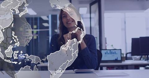Smiling businesswoman at office desk with digital globe overlay and analytics dashboard