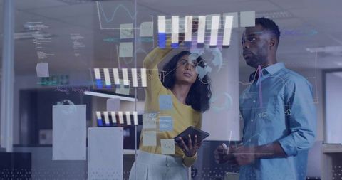 Diverse team collaborating on glass board with sticky notes and data visuals in office