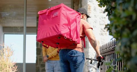 Doorstep delivery courier talking with resident holding bicycle and red insulated backpack