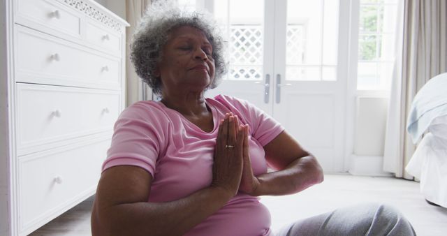 Senior woman practicing meditation in yoga pose at home. Helps to depict wellness, relaxation, and healthy living among older adults. Suitable for use in articles on mental health, mindfulness, senior fitness, and promoting a balanced lifestyle. Ideal for wellness websites, senior living advertisements, and content on self-care.