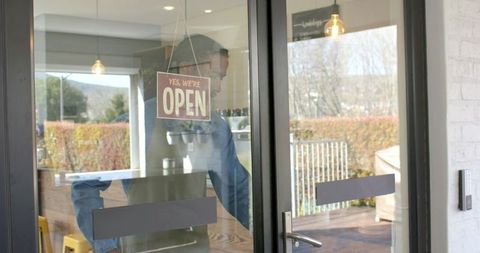 African american barista brewing coffee behind glass door with open sign and patio view