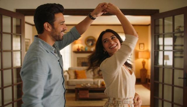 Couple dancing and twirling in cozy living room through open wooden french doors