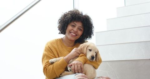 African american woman smiling while cradling golden retriever puppy on marble stairs