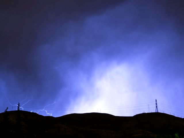Lighting strikes illuminate dark sky behind silhouetted hills and power lines during stormy night. Can be used for topics related to extreme weather, electrical storms, natural phenomena, or power and electricity. Ideal for illustrating articles or presentations on meteorology, environmental issues, or energy supply.