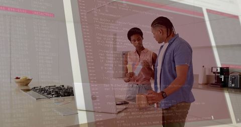 Young professionals collaborating on code using laptop and smartphone in modern kitchen