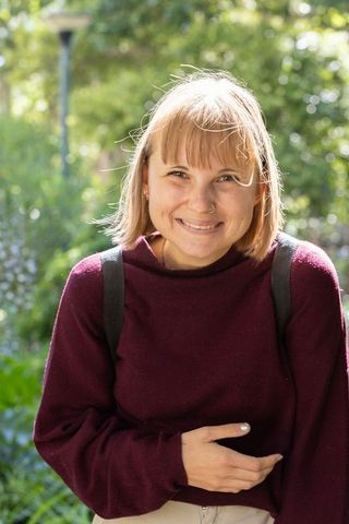 Young woman smiling in sunlit park wearing burgundy sweater with nose ring and backpack