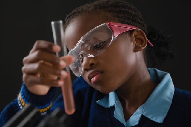 Young schoolgirl wearing safety goggles carefully examining a test tube during a science experiment. Ideal for educational materials, science and technology promotions, and STEM learning resources.