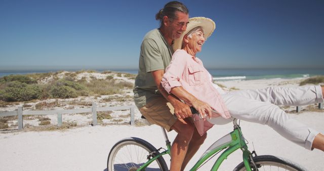 Senior couple enjoying a joyful ride on a green bicycle along a beach path surrounded by sand dunes. They are smiling and embracing an active lifestyle, epitomizing happiness and togetherness. This visual conveys themes of romance, adventure, and retirement. Ideal for marketing materials for travel agencies, senior health products, retirement plans, or advertisements emphasizing outdoor activities and active aging.