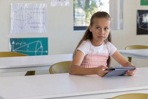 Schoolgirl using tablet in classroom with long white desks, yellow chairs and geometry posters