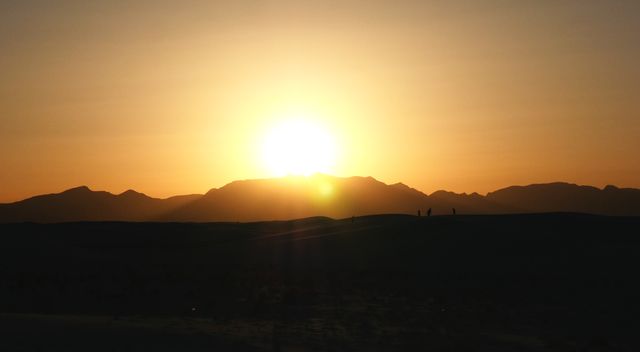Silhouette of a mountain range during sunset with the bright sun dipping below the peaks. Ideal for backgrounds, travel blogs, websites, wallpapers, advertisements meaning to convey peace and natural beauty.