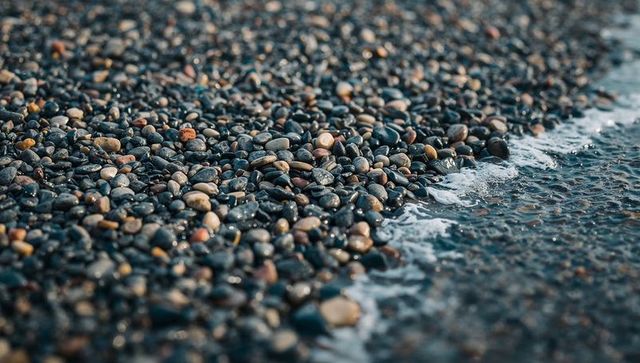 Glinting pebble shoreline with wet smooth stones reflecting light and gentle foam