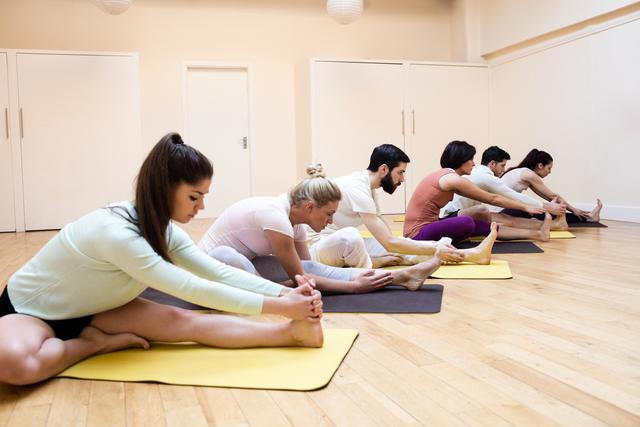 Group of people performing stretching exercise on exercise mat in the fitness studio
