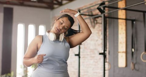 Woman stretching neck before workout in industrial gym wearing headphones and smartwatch