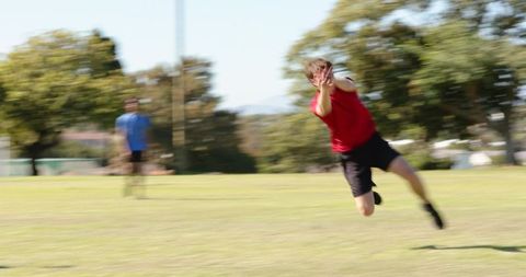 Diverse friends diving and catching football in sunny park mid-air action