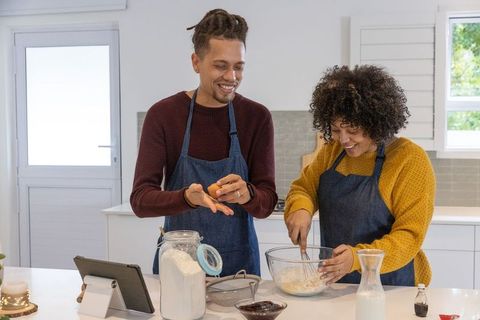 African american couple whisking batter in bright modern kitchen, smiling and laughing