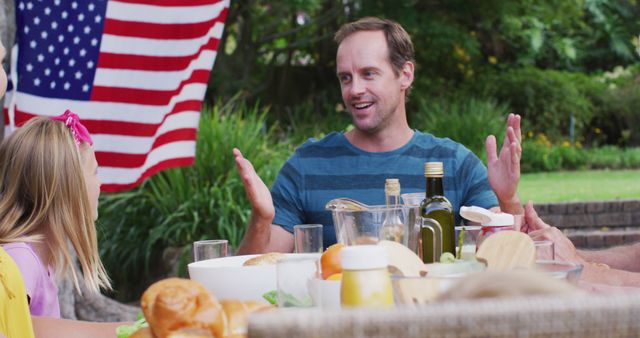 Smiling caucasian man talking during family celebration meal in garden. family celebrating independence day eating outdoors together.