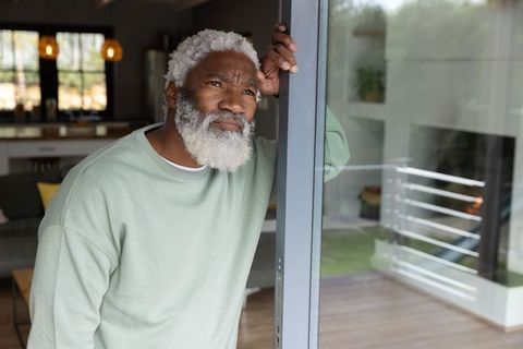 Contemplative senior african american man leaning on sliding door looking out at deck