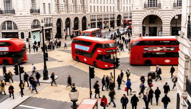 Red double-decker buses blurring through busy london junction with moving pedestrians