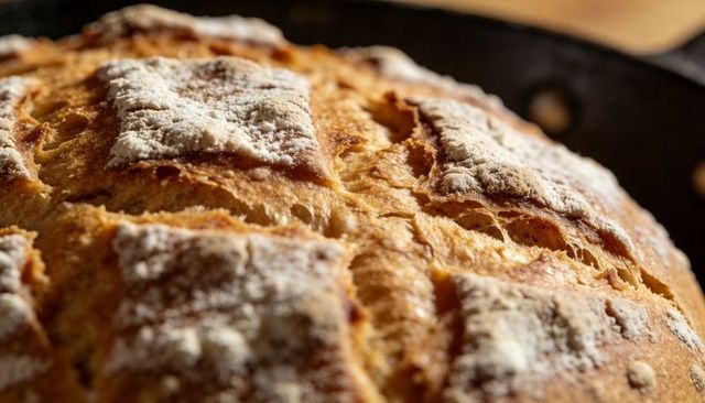 Rustic artisan sourdough loaf with golden cracked crust dusted with flour in cast iron