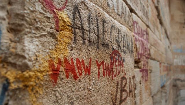 Weathered graffiti on stone wall along narrow alleyway, dripping paint and mortar texture