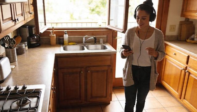 Young woman listening to music and checking smartphone in sunlit kitchen