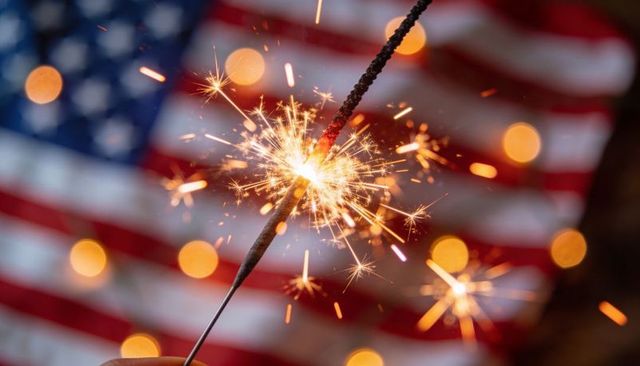 Holding sparkler in front of american flag with warm bokeh for patriotic celebration