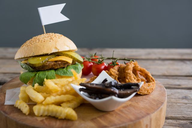 Perfect for illustrating fast food menus, restaurant advertisements, or food blogs. The image showcases a mouth-watering burger with fresh lettuce, cheese, and pickles, accompanied by crinkle-cut fries, crispy onion rings, and a side of grilled mushrooms. The rustic wooden board and table add a homely touch, making it ideal for promoting comfort food or casual dining experiences.