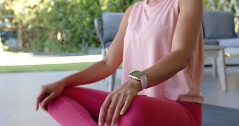 African woman sitting cross-legged on sunlit patio practicing yoga wearing smartwatch