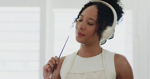 African american woman painting while listening to headphones in bright home studio