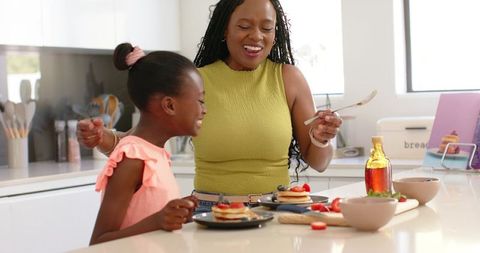 African american mother and daughter making pancakes at bright contemporary kitchen island
