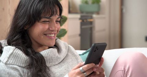 Woman Relaxing on Sofa Smiling at Smartphone in Comfortable Living Room