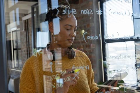 Female developer writing code on glass board in modern office