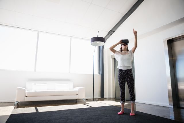 Businesswoman using VR headset in modern, brightly lit office space. Ideal for illustrating concepts of innovation, digital transformation, and the integration of technology in professional environments. Suitable for tech articles, business marketing materials, and workplace innovation campaigns.